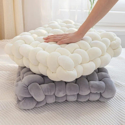 Coussins décoratifs en tissu doux, l'un blanc et l'autre gris, posés sur un tapis texturé dans un salon lumineux