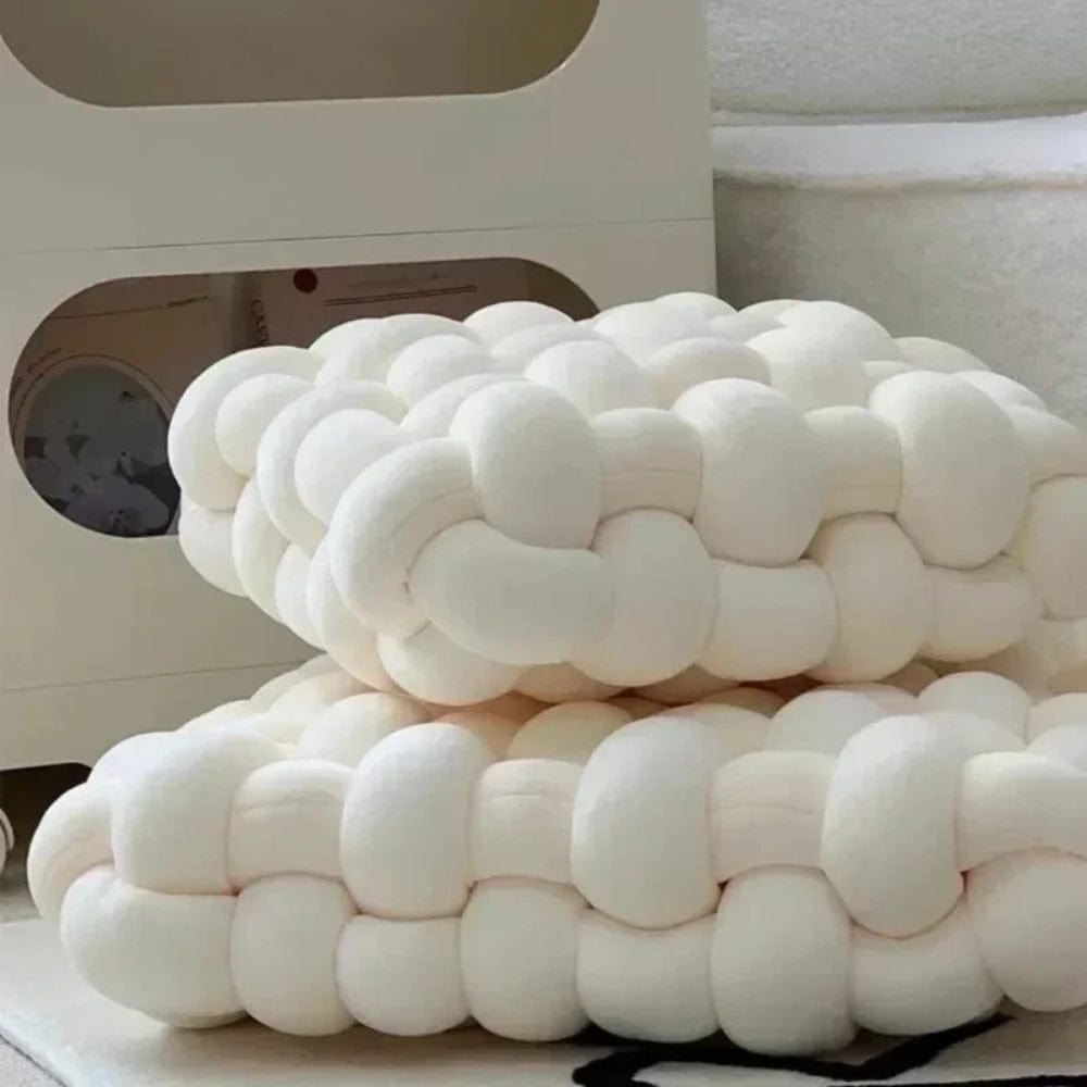 Coussins décoratifs en tissu blanc, forme nouée, posés sur un tapis dans un salon moderne