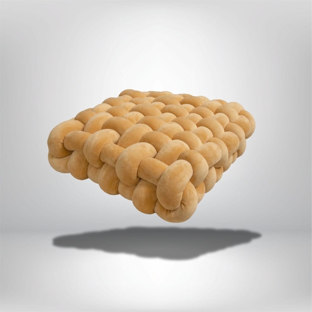 Coussin décoratif en velours beige, aux formes arrondies, posé en suspension sur fond neutre, idéal pour un canapé moderne