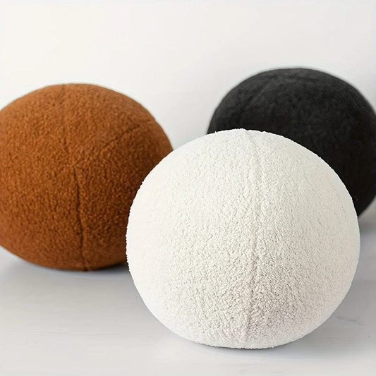 Trois coussins ronds en tissu doux, de couleurs brune, blanche et noire, posés sur une surface claire