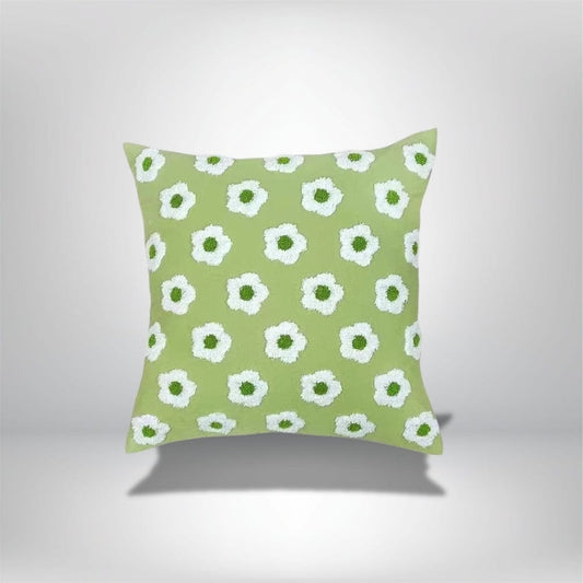 Coussin décoratif vert avec motifs floraux blancs et centres verts, posé sur un fond neutre