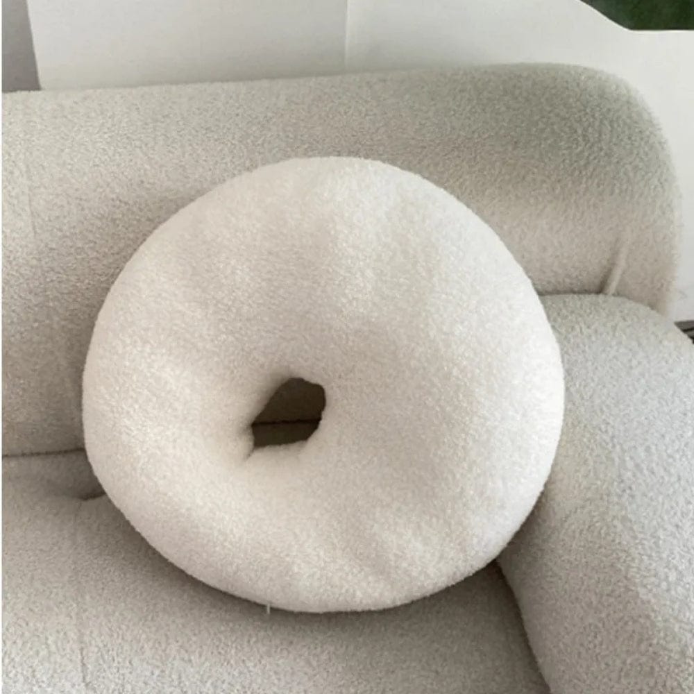 Coussin décoratif en forme de donut, couleur blanche, en matière douce, posé sur un canapé beige