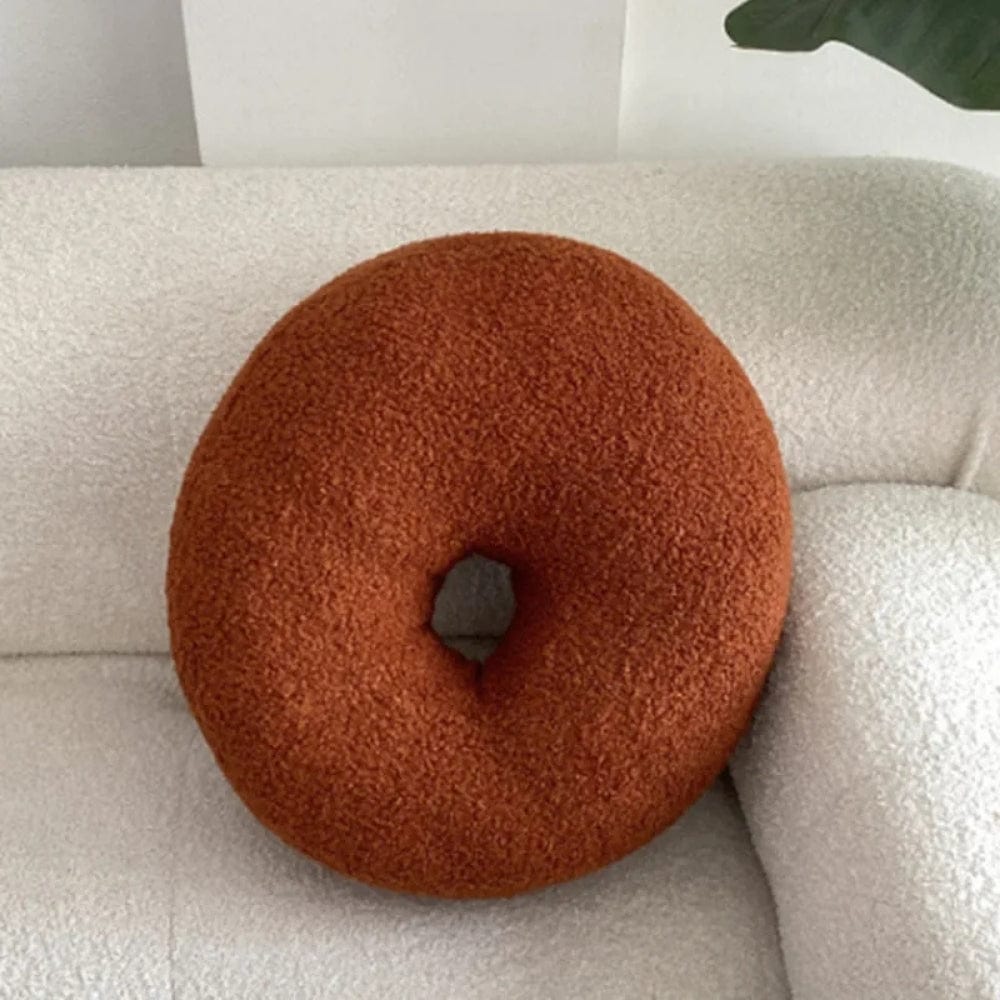 Coussin décoratif en forme de donut, couleur orange, posé sur un canapé blanc texturé