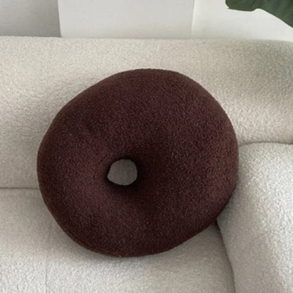 Coussin décoratif en forme de donut, couleur marron, posé sur un canapé blanc en tissu doux
