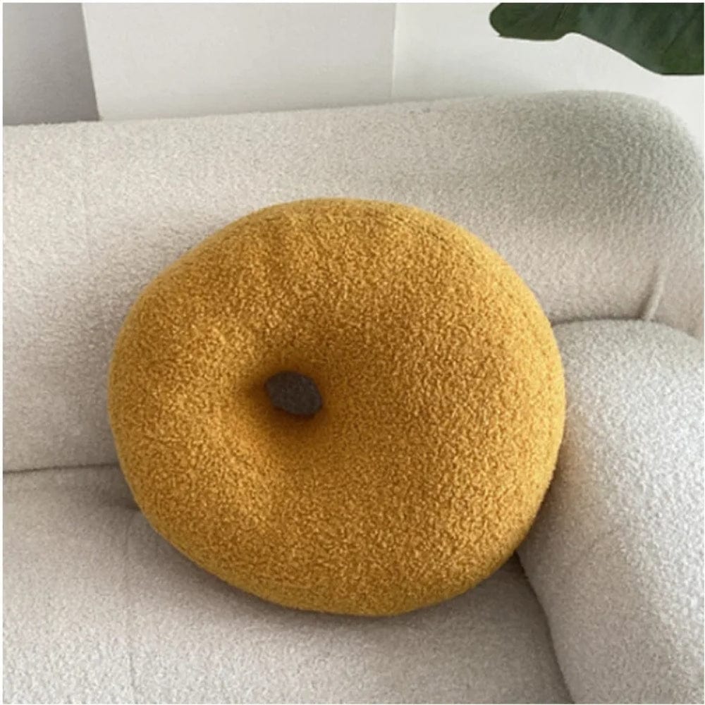 Coussin décoratif en forme de donut, couleur jaune, posé sur un canapé blanc en tissu doux