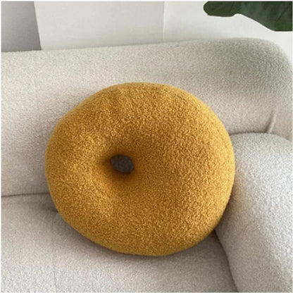 Coussin décoratif en forme de donut, couleur jaune, posé sur un canapé blanc en tissu doux