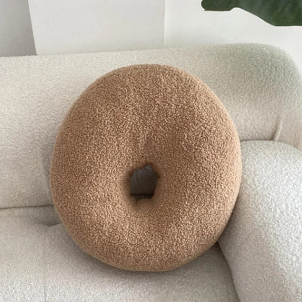 Coussin décoratif en forme de donut, couleur beige, en matière douce, posé sur un canapé clair