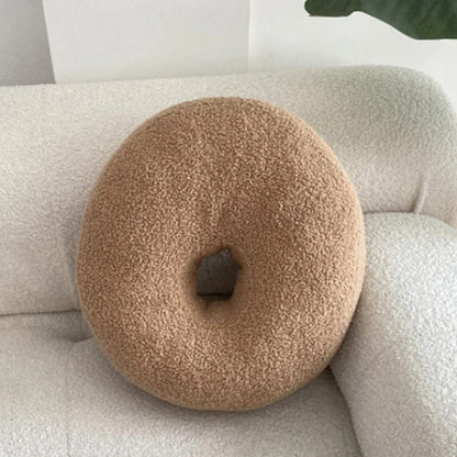 Coussin décoratif en forme de donut, couleur beige, en matière douce, posé sur un canapé clair