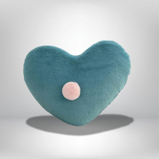 Coussin déco en forme de cœur bleu avec un pompon rose, posé sur une surface neutre