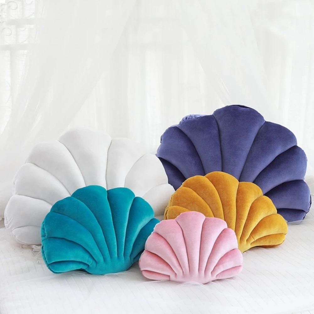Coussins décoratifs en forme de coquillage aux couleurs variées, posés sur un lit blanc, ajoutant une touche ludique