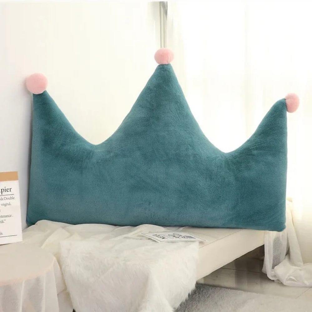 Coussin déco en forme de couronne, en velours bleu avec pompons roses, posé sur un canapé