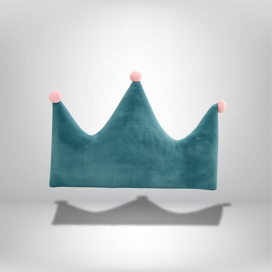 Coussin décoratif en forme de couronne, en velours bleu avec des pompons roses, posé sur un fond neutre