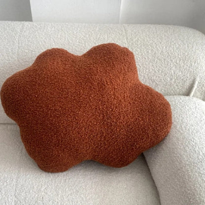 Coussin en forme de nuage, couleur rouille, en matière douce, posé sur un canapé blanc texturé