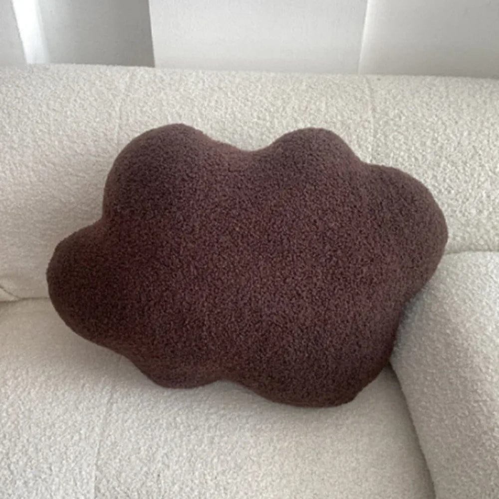 Coussin en forme de nuage marron posé sur un canapé blanc texturé, ajoutant une touche déco chaleureuse