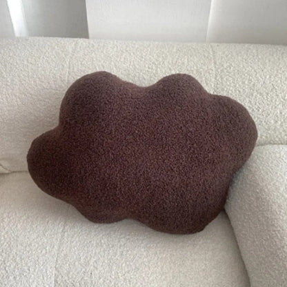 Coussin en forme de nuage marron posé sur un canapé blanc texturé, ajoutant une touche déco chaleureuse