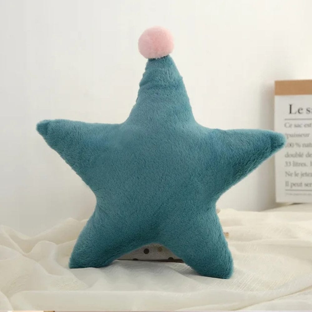 Coussin décoratif en forme d'étoile, en velours bleu, avec un pompon rose, posé sur un tissu léger