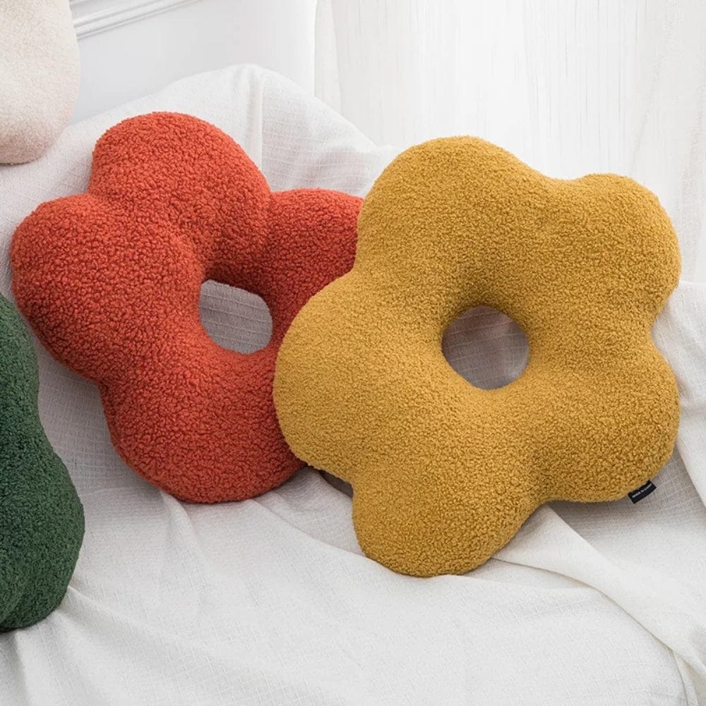 Coussins décoratifs en forme de fleur, orange et jaune, posés sur un canapé blanc