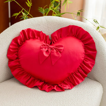 Coussin décoratif en forme de cœur rouge, avec volants et nœud, posé sur un canapé beige