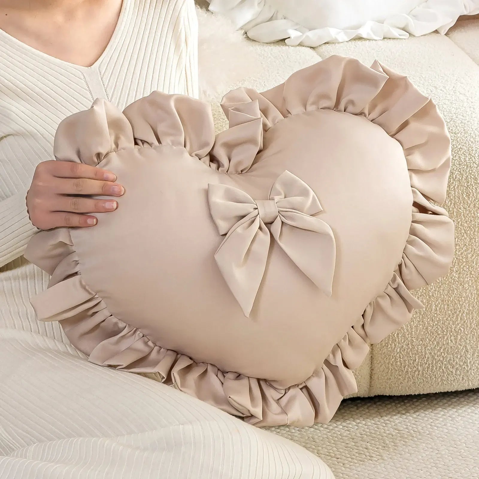 Coussin décoratif en forme de cœur beige avec volants et nœud, posé sur un canapé clair
