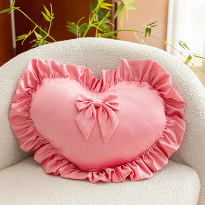 Coussin décoratif en forme de cœur rose avec volants, posé sur un canapé clair, apportant une touche romantique