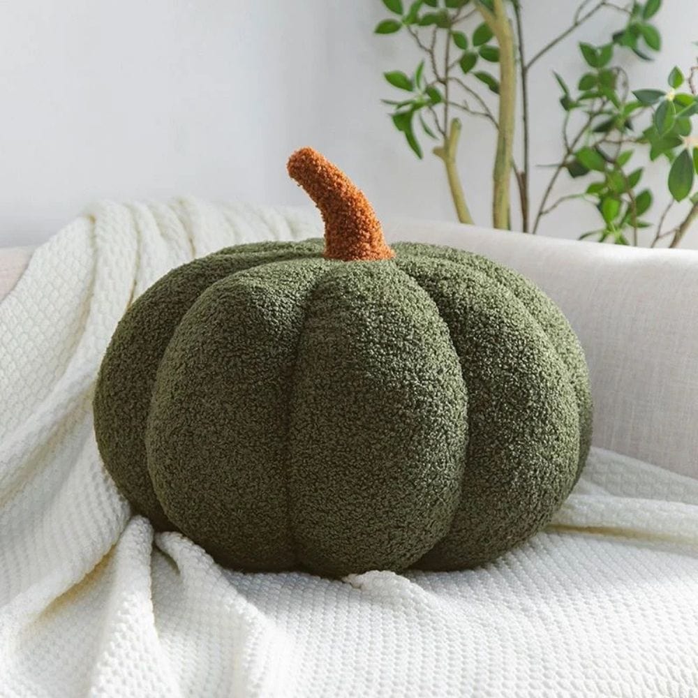 Coussin décoratif en forme de citrouille, vert avec une tige orange, posé sur un canapé beige