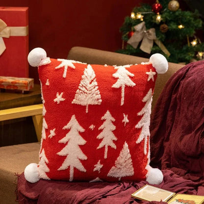 Coussin décoratif rouge avec motifs de sapins blancs, posé sur un canapé, apportant une touche festive et chaleureuse