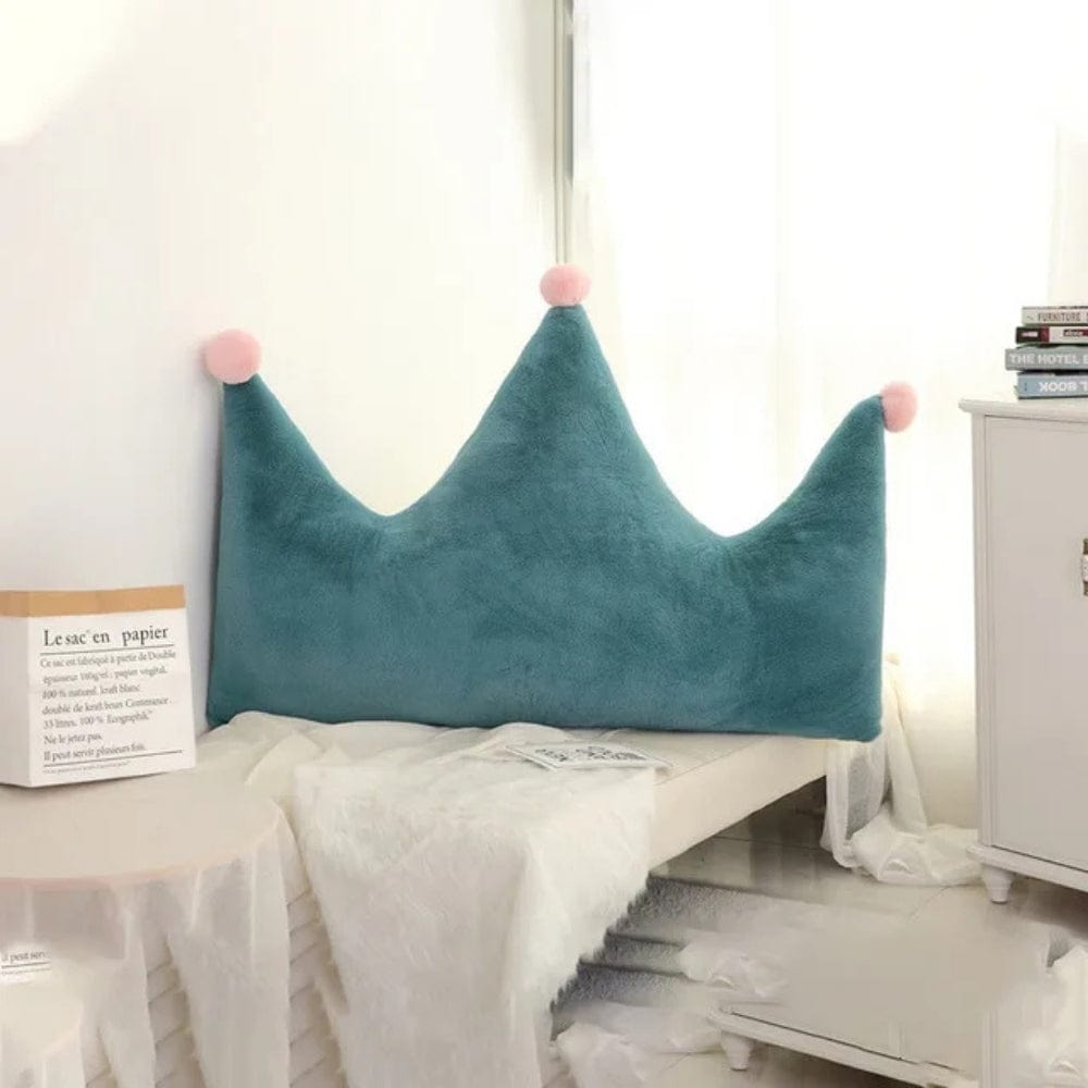 Coussin déco en forme de couronne, en velours bleu avec pompons roses, posé sur un lit décoré