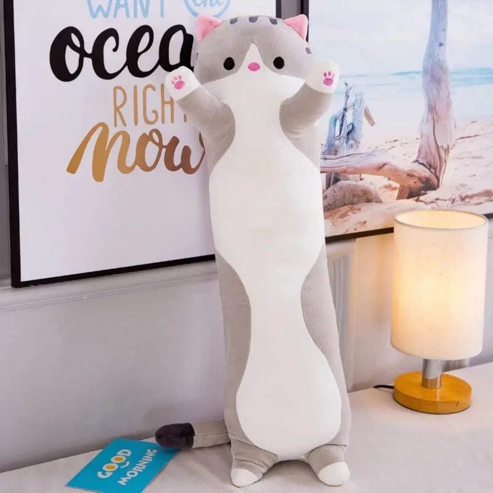 Coussin long en forme de chat, aux couleurs grises et blanches, décorant un lit avec une ambiance chaleureuse