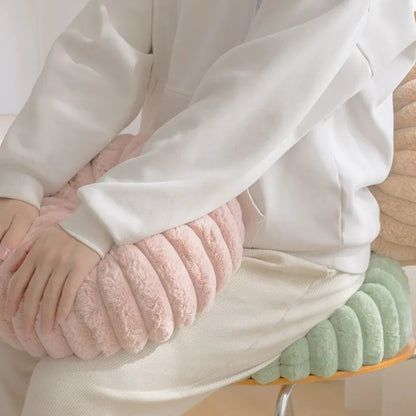 Coussin déco moelleux en velours rose, posé sur une chaise, avec des coussins vert et beige à proximité