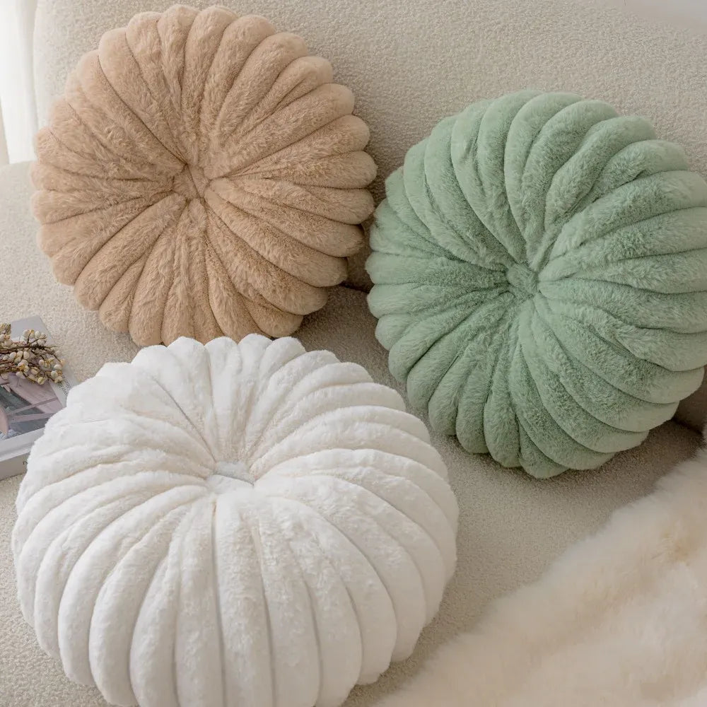 Trois coussins décoratifs ronds en velours moelleux, beige, vert et blanc, posés sur un canapé doux