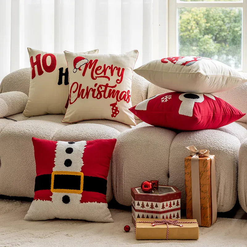 Coussins décoratifs aux motifs de Noël, rouges et blancs, disposés sur un canapé confortable avec des cadeaux