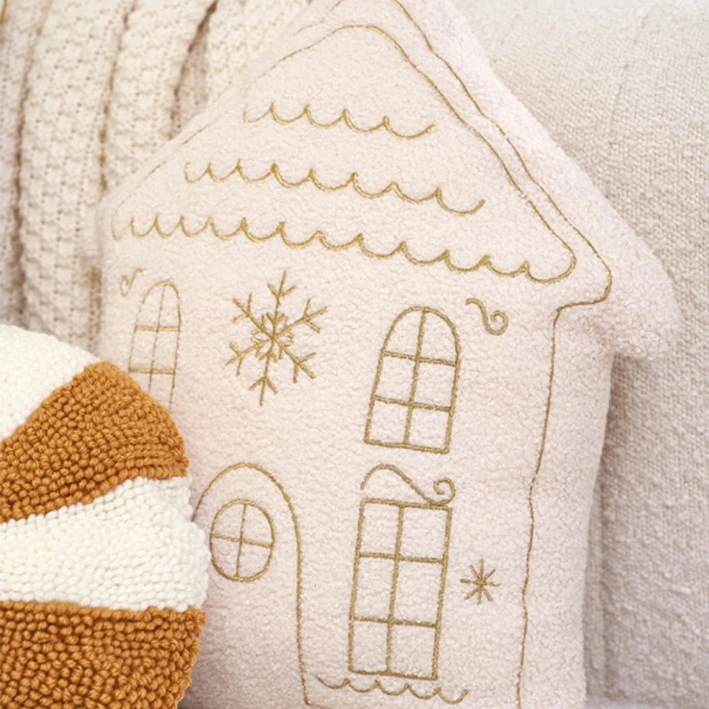Coussin décoratif en forme de maison rose avec motifs dorés, posé sur un canapé beige pour une ambiance chaleureuse