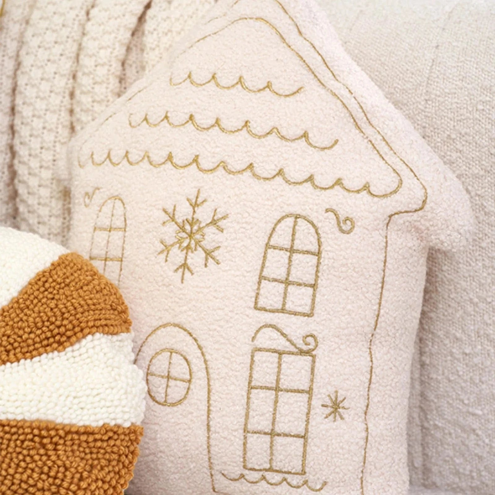 Coussin décoratif en forme de maison rose avec motifs dorés, posé sur un canapé beige pour une ambiance chaleureuse
