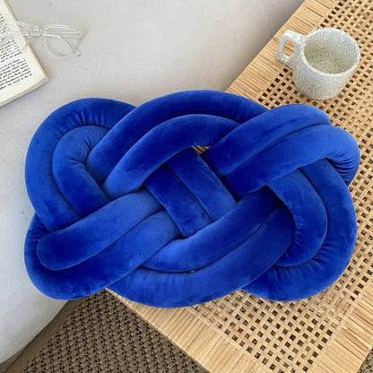 Coussin décoratif en velours bleu en forme de nœud, posé sur une table en bois, à côté d'une tasse