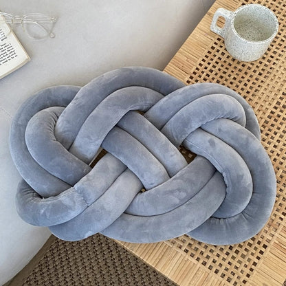 Coussin décoratif en velours gris en forme de nœud, posé sur une table en bois dans un salon moderne