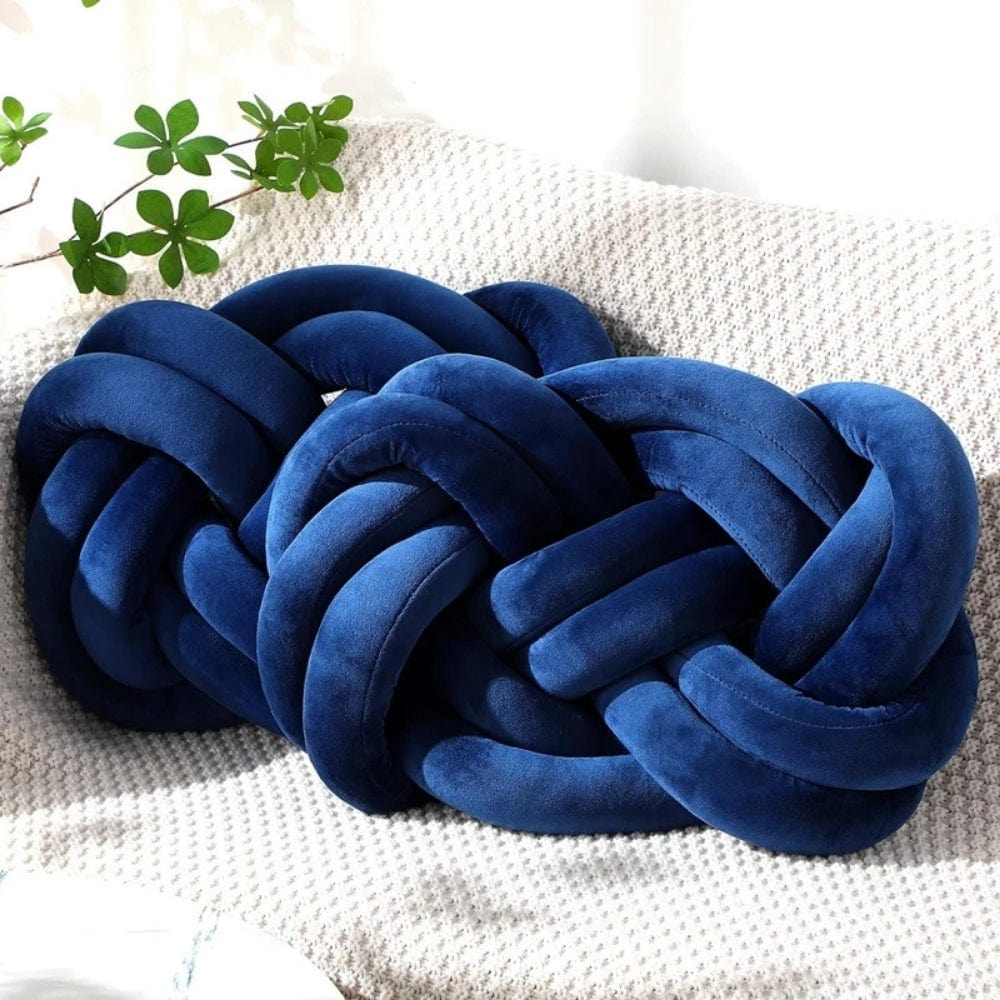 Coussin décoratif en velours bleu en forme de noeud, posé sur un canapé à texture claire