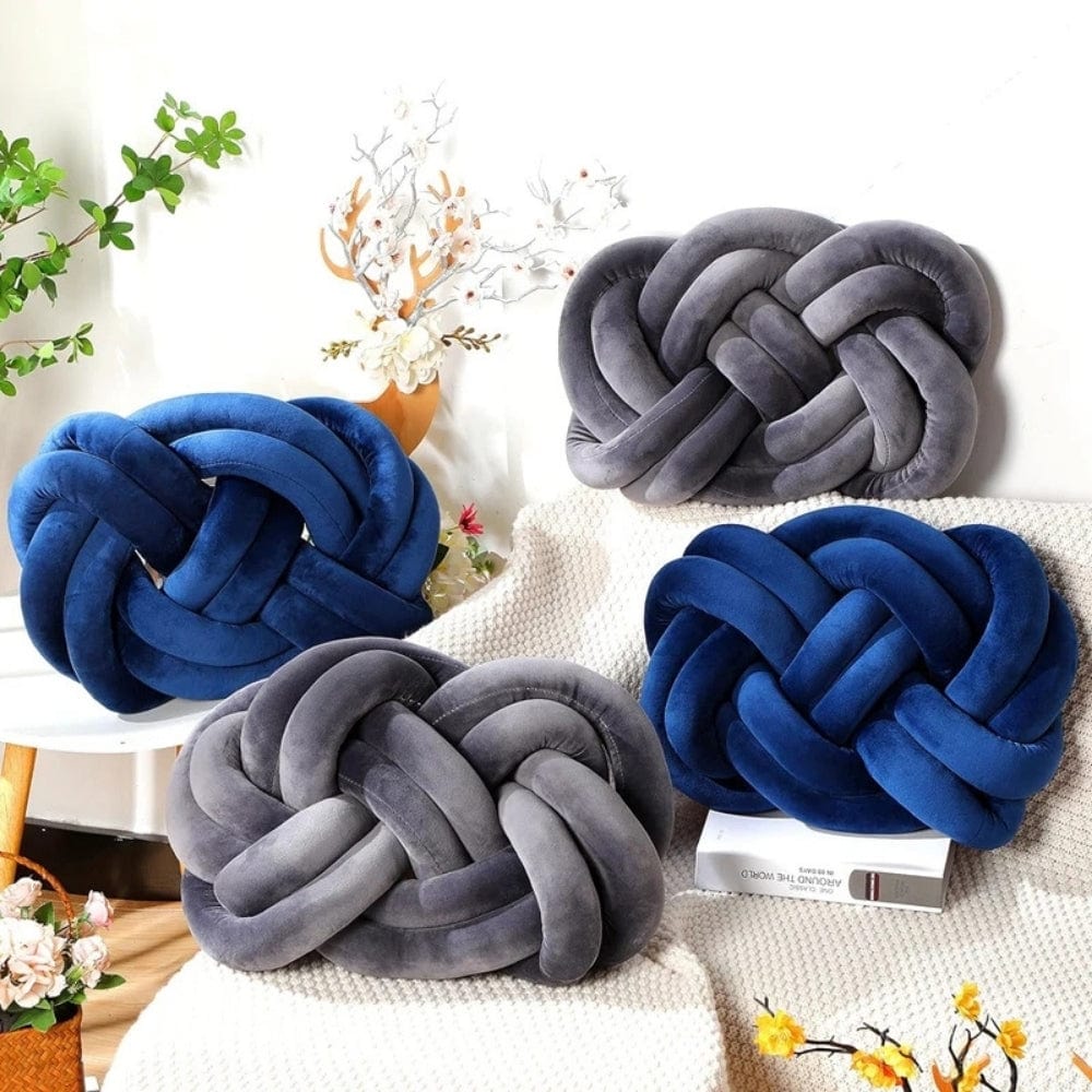 Coussins décoratifs en velours bleu et gris en forme de noeud, posés sur un canapé avec un plaid