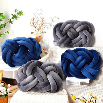 Coussins décoratifs en velours bleu et gris en forme de noeud, posés sur un canapé avec un plaid
