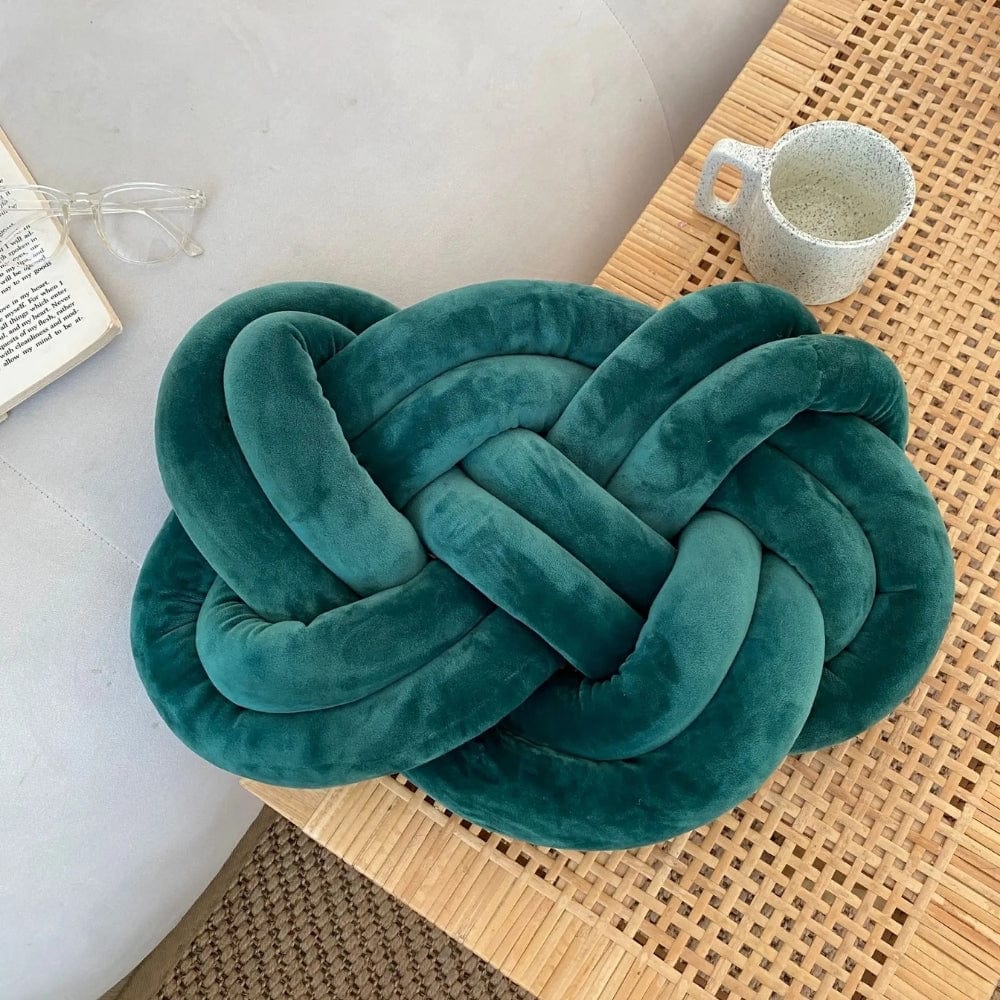 Coussin décoratif en velours vert émeraude en forme de nœud, posé sur une table en bois dans un salon