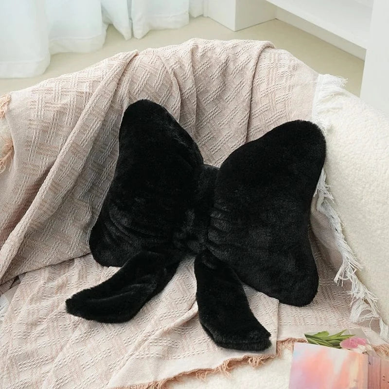 Coussin décoratif en velours noir en forme de nœud papillon sur un canapé avec un plaid beige