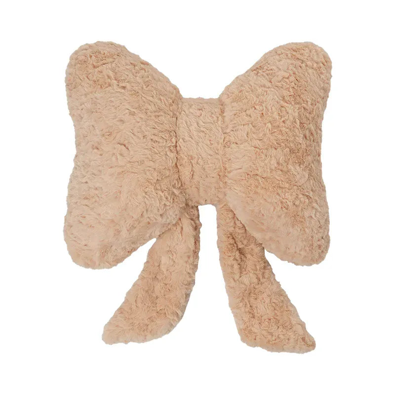 Coussin décoratif en forme de nœud papillon, couleur beige, texture douce, posé sur un canapé moderne