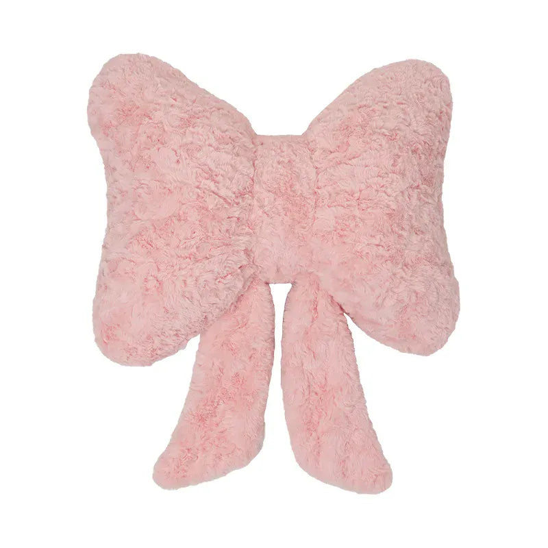 Coussin décoratif en forme de nœud papillon, en peluche rose, posé sur un canapé moderne