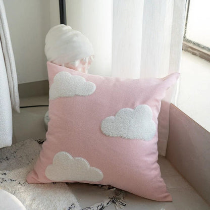 Coussin décoratif rose avec des motifs de nuages blancs, posé sur un tapis près d'une fenêtre