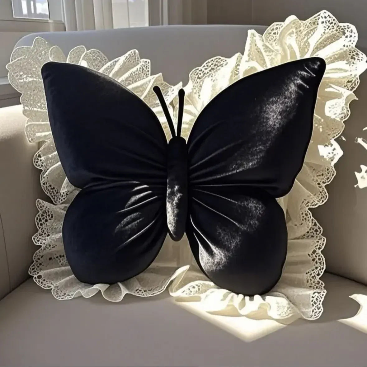 Coussin décoratif en forme de papillon noir avec un liseré en dentelle blanche, posé sur un canapé