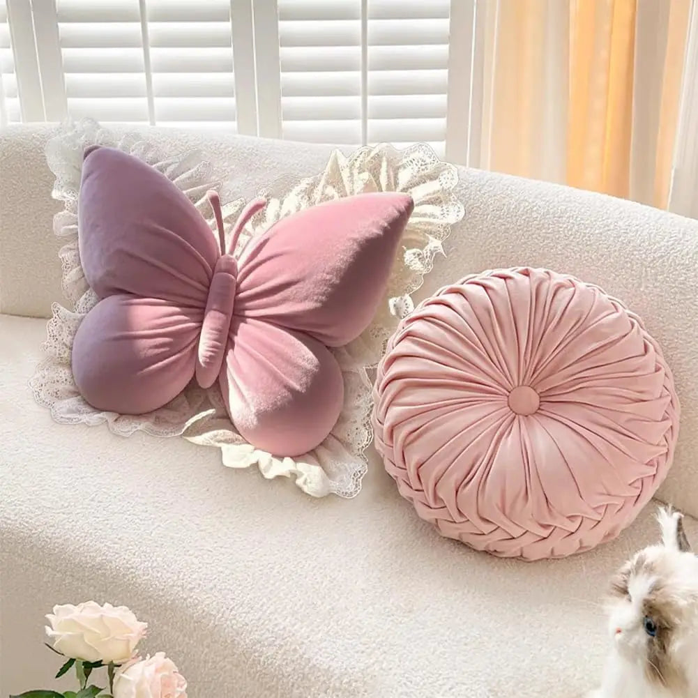 Coussin déco en forme de papillon rose sur un canapé, avec des détails en dentelle et un coussin rond assorti