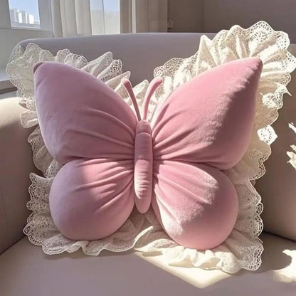 Coussin décoratif en forme de papillon rose avec une bordure en dentelle, posé sur un canapé