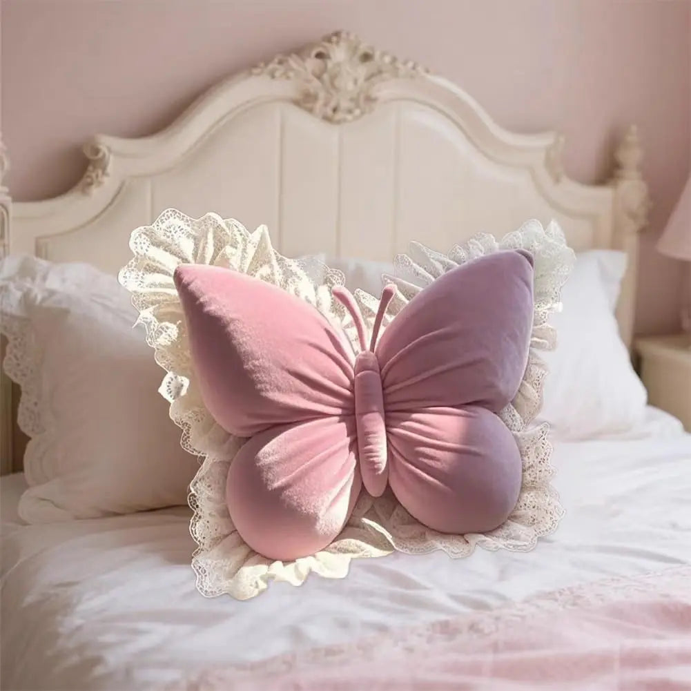 Coussin décoratif en forme de papillon rose avec des détails en dentelle, posé sur un lit aux draps clairs