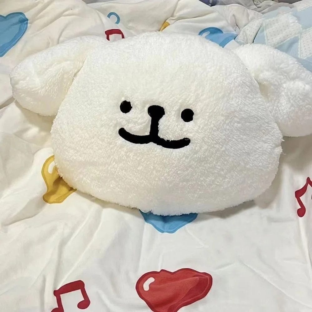 Coussin décoratif en forme de chien blanc avec un visage souriant, posé sur un lit aux draps colorés