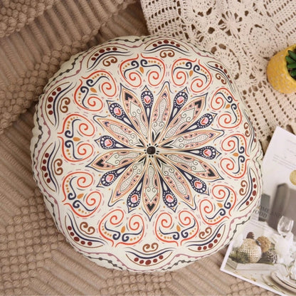 Coussin pouf de sol rond avec un motif floral coloré sur un fond crème, posé sur un plaid beige