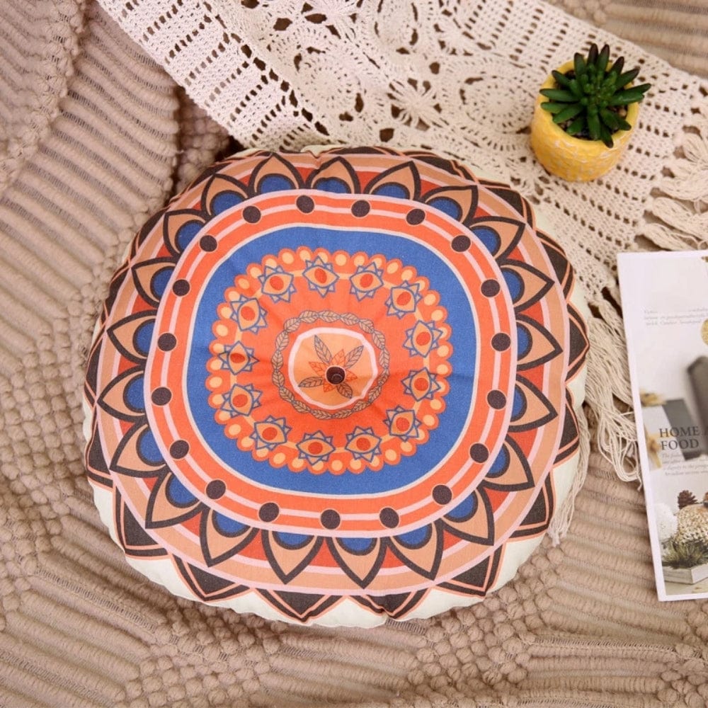 Coussin pouf rond aux motifs colorés orange et bleu, posé sur un tapis texturé dans un salon chaleureux